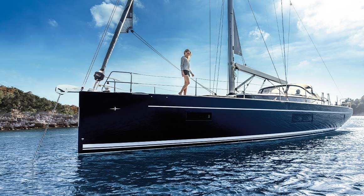 Side view of a boat on calm blue water with a woman on board and the coast in the background.
