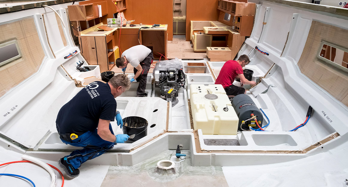Three men work on installations in the boat's hull.