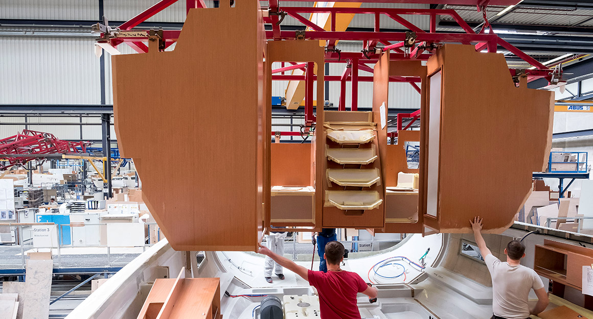 Finished cabin module, held by crane and two workers.