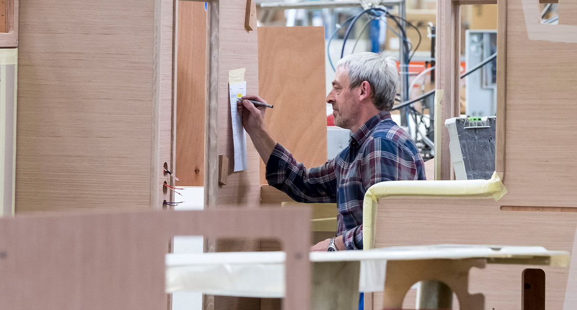 View through several wooden module parts of a worker in a shirt taking notes.