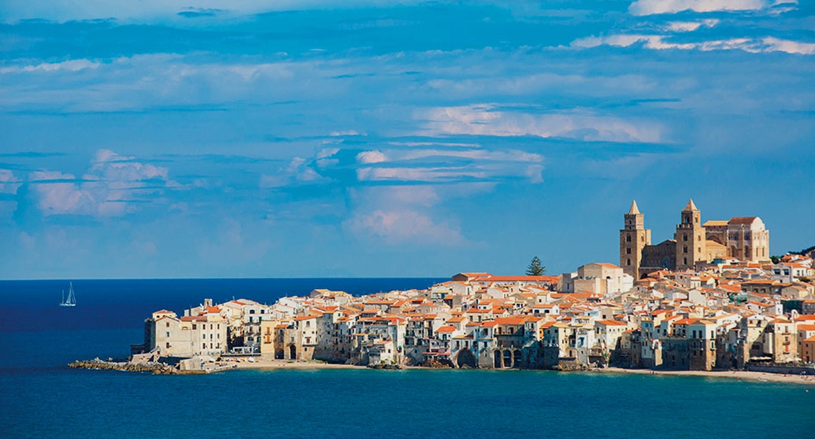 View of the deep blue bay of Cefalù with a Mediterranean town in the background.