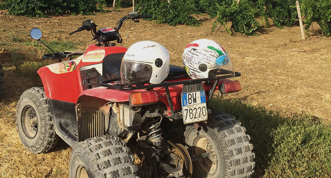 A red quad bike from behind with two helmets on the seat on dry ground.