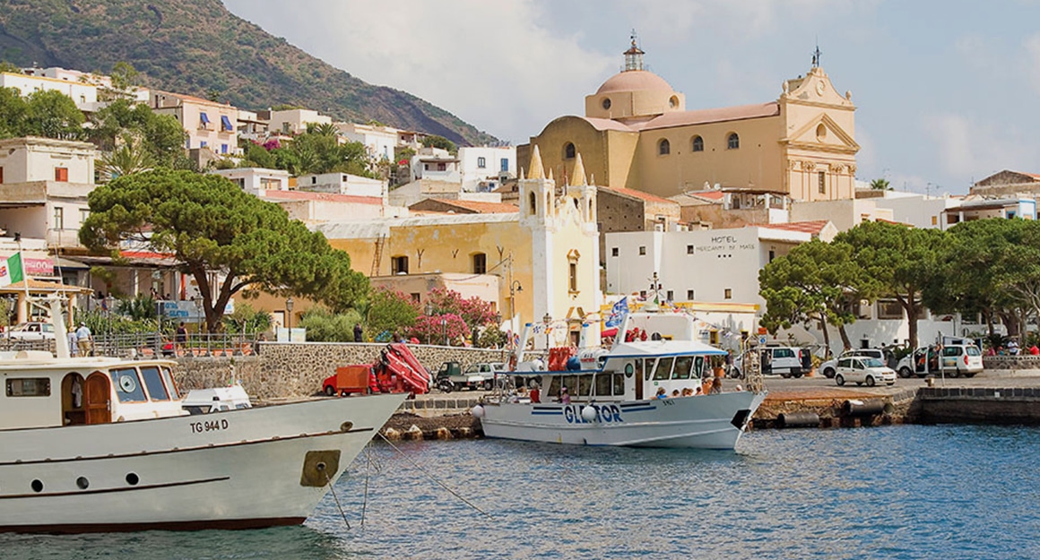 Two small boats moored on the shore of a small, colourful Sicilian town.