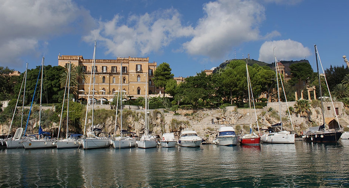 A quiet bay with a row of boats and a hilly coastal town in the background.