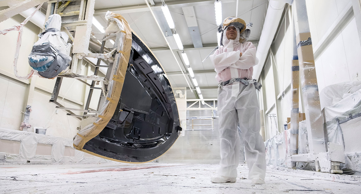 Man in white work clothes in the shipyard hall laminating the first layer of the deck.