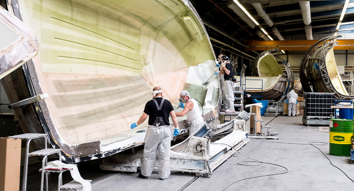 View of the shipyard with several boat moulds and 4 men working on them.
