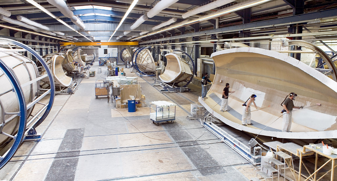 View from above into the large hall with numerous boat hulls and workers.