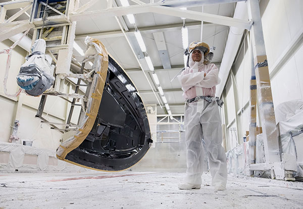 Man in white work clothes in the shipyard hall laminating the first layer of the deck.