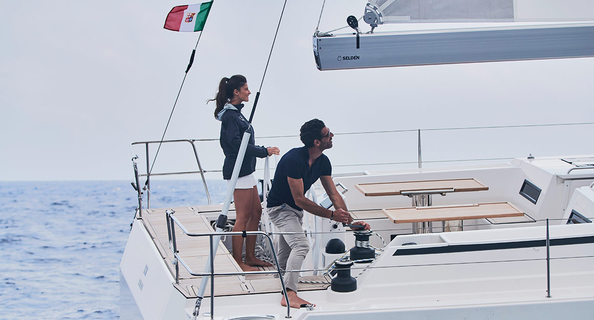 A woman and a man on a small sailing boat hauling in the sail with a furling mainsail.