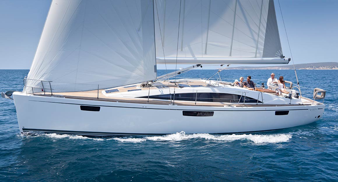 A sailing boat with a furling mainsail on the sea with four people on board.