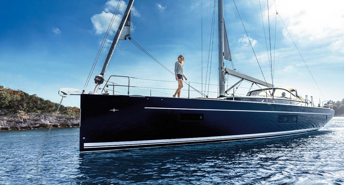 A sailing boat with a furled sail on the sea with the coast in the background.