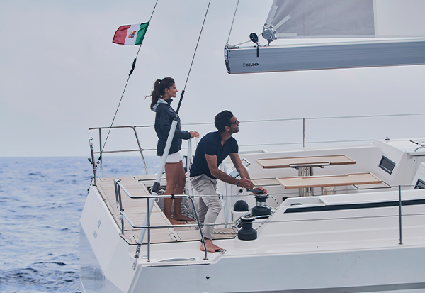 A woman and a man on a small sailing boat hauling in the sail with a furling mainsail.