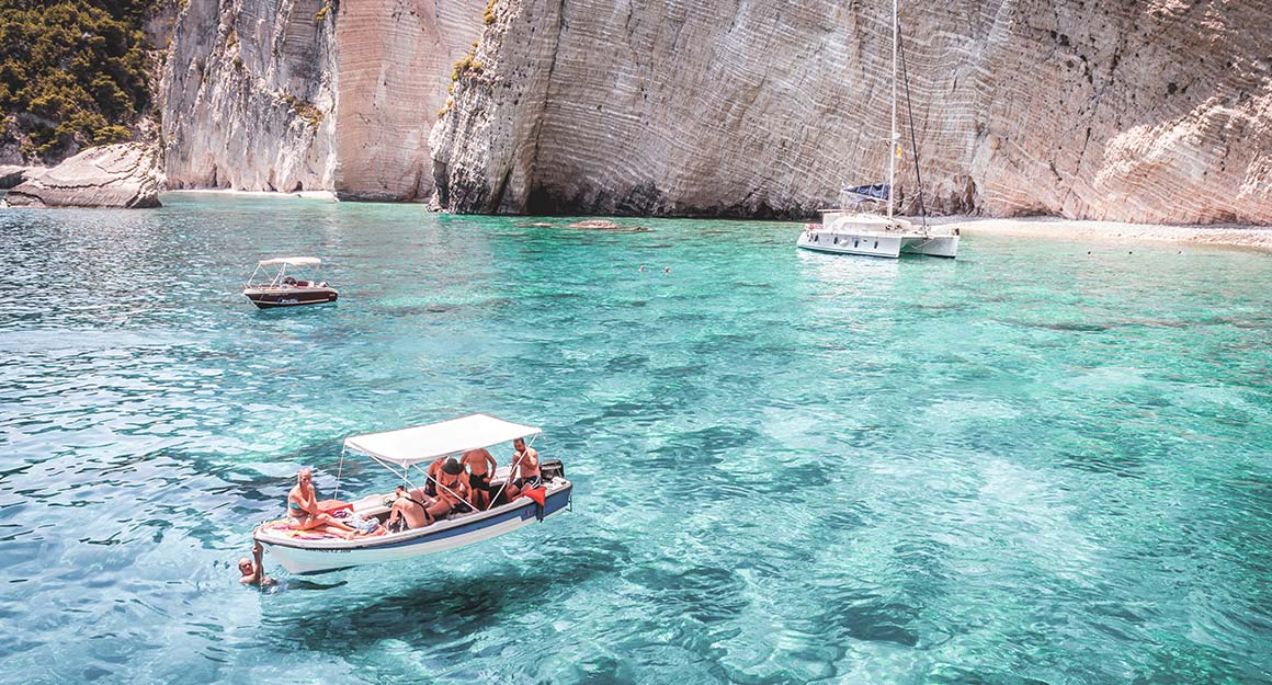 Clear light blue water and boats floating on it on a sunny day with a cliff in the background.