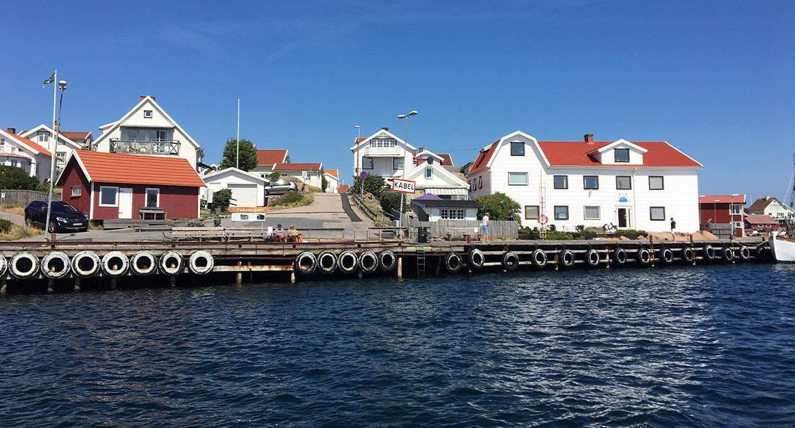 View of promenade with deep blue water and idyllic coastline with a few white houses and people.
