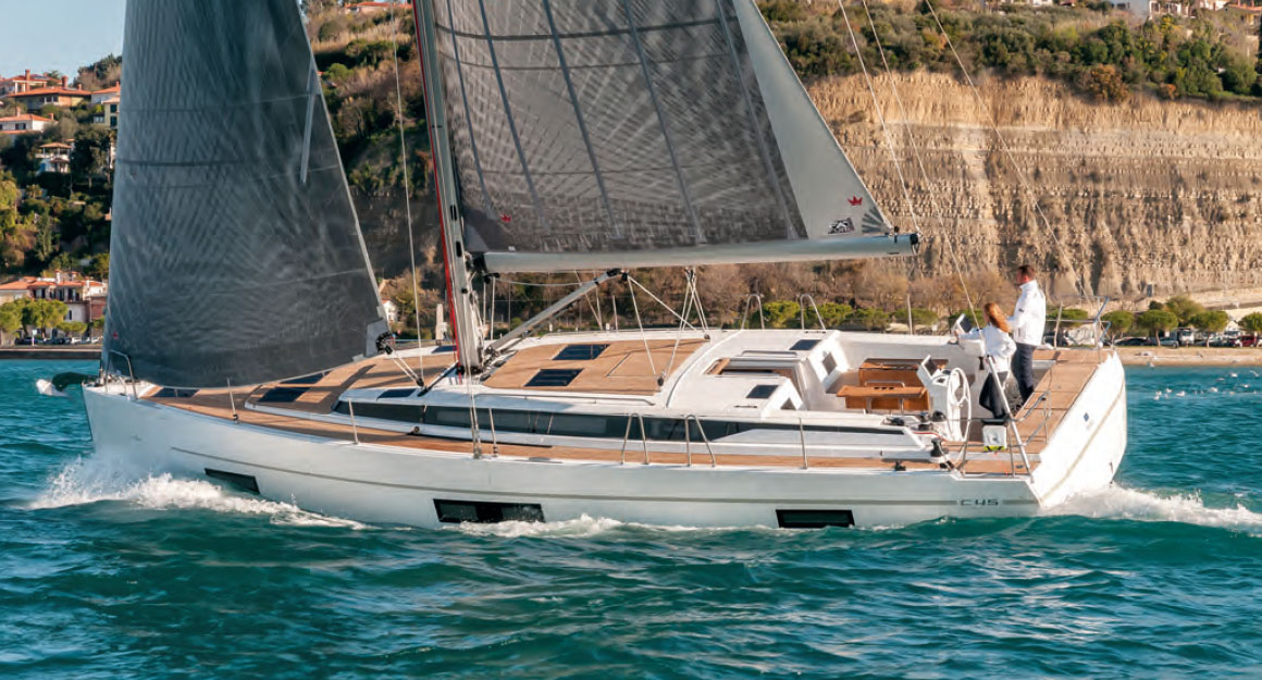 Sailboat from the side on the water with a steep cliff in the background.
