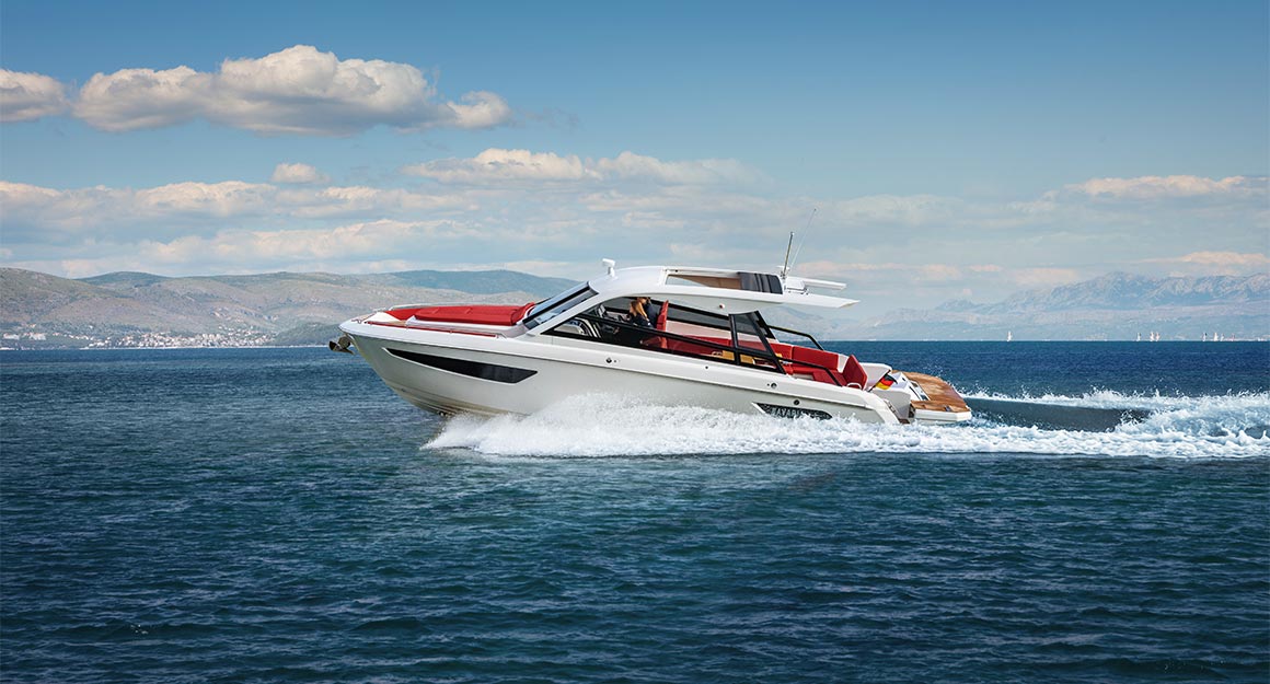 Side view of the BAVARIA VIDA travelling on the water with the coast on the horizon.