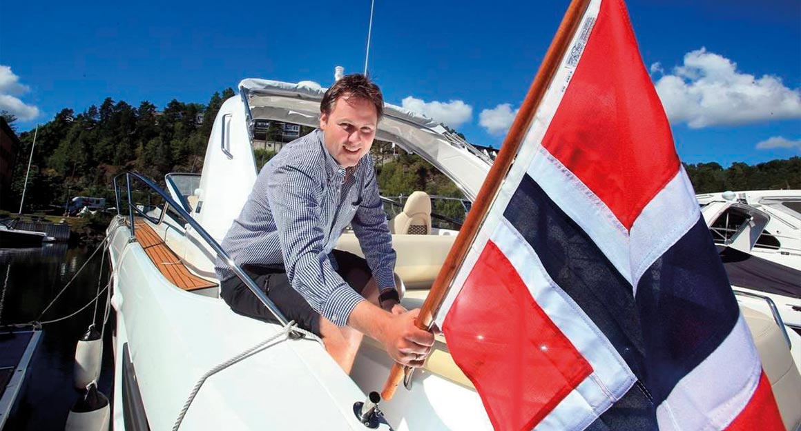 Middle-aged man in a shirt with a Norwegian flag in his hand on a motorboat.