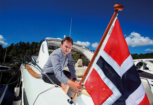 Middle-aged man in a shirt with a Norwegian flag in his hand on a motorboat.